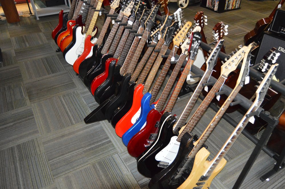 Row of electric guitars in various colors lined up on a wall rack