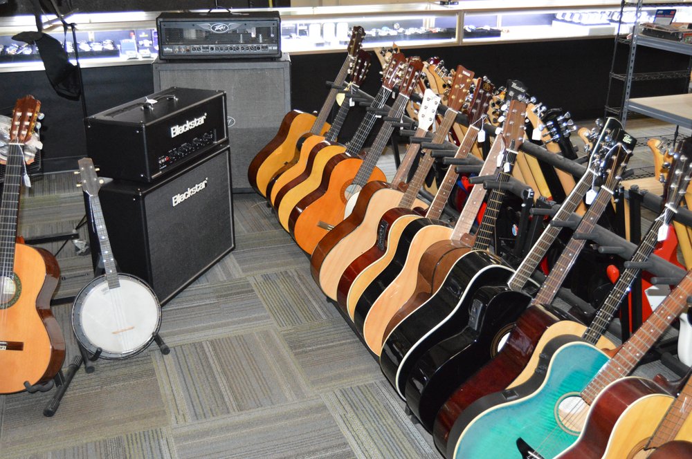 Acoustic and electric guitars standing in floor racks next to guitar amplifiers
